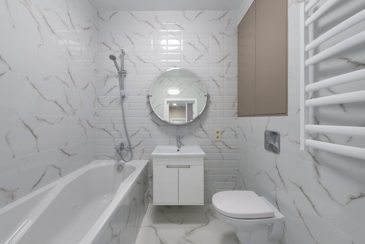Elegant bathroom with marble tiles, round mirror, and white fixtures.